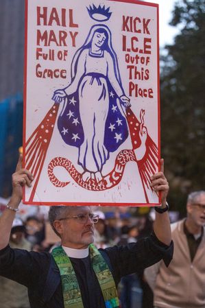 A protester holds a hand-painted placard depicting the Virgin Mary with text reading "Hail Mary Full of Grace Kick I.C.E. Out of This Place" during a demonstration in Foley Square against U.S. Immigration and Customs Enforcement (ICE) operations following the shooting of Oscar Bergal in Marble Hill, Bronx.