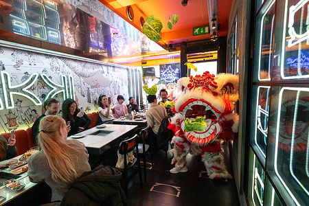 Performers in lion costume throw lettuce to the restaurant customers. Performers in traditional lion costumes took part in a lion dance performance during the Chinese New Year celebrations in Chinatown, London. Accompanied by drumming and cymbals, the lions visited shop entrances where business owners hung lettuce above the doors as part of the traditional ritual. The lion leapt to grab the lettuce before spitting it out to symbolically scatter good fortune, blessings and prosperity to the businesses and gathered crowds, marking the start of the Lunar New Year festivities.