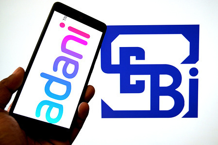 In this photo illustration, an Adani Group logo is seen displayed on a smartphone with a SEBI (Securities and Exchange Board of India) logo in the background.