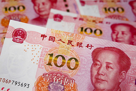 In this photo illustration, a 100 - yuan Renminbi banknote is in the foreground. The details including the national emblem, "People's Bank of China" in Chinese, golden "100" denomination, and portrait are prominent, with other banknotes in the background.