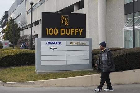 A person walks past a sign of the New York Community Bank Plaza office in the neighborhood of Hicksville in Nassau County, Long Island, New York.