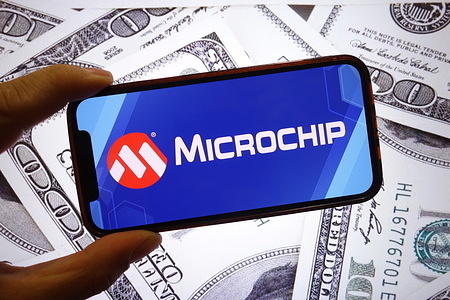 In this photo illustration, the Microchip Technology company logo is seen displayed on a smartphone screen with United States dollar banknotes in the background.
