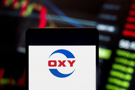 In this photo illustration, the American company engaged in hydrocarbon exploration, Occidental Petroleum Corporation (OXY, NYSE: OXY), logo seen displayed on a smartphone with an economic stock exchange index graph in the background.