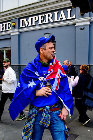 A male anti-immigration protester wrapped in an Australian flag seen on the street outside the Imperial Hotel on Spring Street during rallies. Thousands marched through the CBD in two opposing rallies. Fewer than 500 nationalist, anti-immigration protesters gathered near State Parliament while more than 5,000 counter-demonstrators led by Indigenous activists, pro-Palestine groups, anti-war campaigners, climate activists and socialist organisations filled the streets. Police declared a designated area, deployed squads, mounted units and used crowd-control measures to keep the groups apart around Spring Street and Parliament House. Tensions flared but officers contained the protests preventing major clashes in the city.