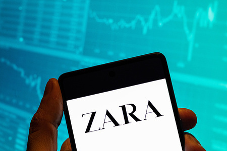 In this photo illustration, the Spanish multinational clothing design retail company by Inditex, Zara, a logo is seen displayed on a smartphone with an economic stock exchange index graph in the background.