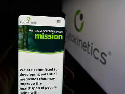 In this photo illustration, a person is holding a smartphone with the webpage of biopharmaceutical company Cytokinetics Inc. on screen in front of logo.