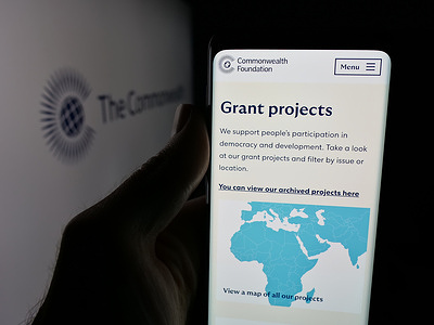 In this photo illustration, a person is holding a smartphone with the webpage of institution Commonwealth Secretariat on screen in front of logo.