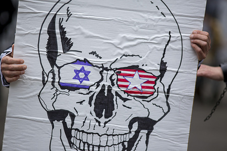 A protester holds a placard with a skeleton drawn on it and the flags of Israel and the United States in its eyes, during a demonstration organized by the Solidarity Network Against the Occupation of Palestine that marched through the streets of Madrid to denounce "the genocide in Palestine" and the arms trade with Israel.