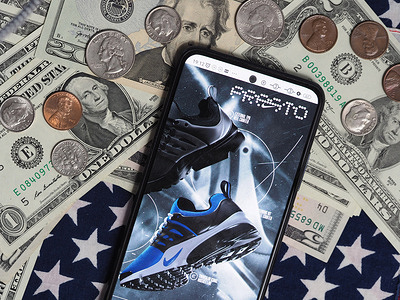 In this photo illustration, a Presto (Nike) advertisement seen displayed on a smartphone with United States Dollar notes and coins in the background.