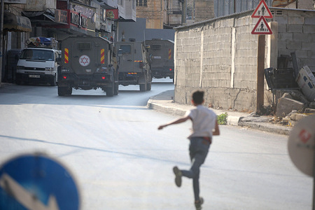A Palestinian throws stones at the Israeli military vehicles during a raid at the entrance to the Old City of Nablus in the West Bank. Israeli soldiers launched a military operation. During the raid, Palestinian vehicles were stopped, their IDs were checked, homes were searched, and a young man was arrested.