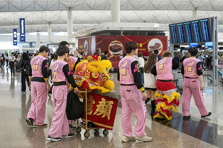 Lion dancers perform the traditional "Cai Qing" (Plucking the Greens) ritual during the Lunar New Year celebrations at Hong Kong International Airport. The yellow and red lion is seen at the shopfront interacting with traveller to bring them good luck and prosperity.