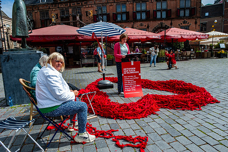 A woman making red ribbons is seen looking at the camera. During this week and until tomorrow, residents of Nijmegen read out during day and night, the names of the people who died in Gaza; both the Israeli victims of 7 October 2023 and the Palestinian victims of then and afterwards.