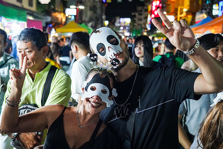 Tourists wearing ghost face-mask pose for photo as they celebrate Halloween. In Bangkok Thailand at Khao San Road, a night filled with costumes, festivities, and a touch of mystery.