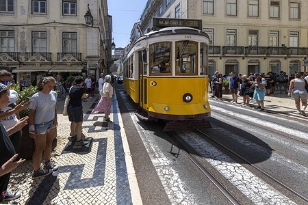 People walk near a tram running through one of the streets in the Baixa district. Portuguese summers are marked by intense heat waves, with temperatures exceeding 35°C, affecting the daily lives of residents and tourists alike. Between cobbled streets and century-old trams, the city adapts to the extreme heat while authorities warn of health risks and increased energy demand.