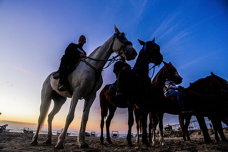 Palestinians ride their horses along the beach during sunset in Gaza City.