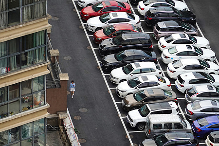 A pedestrian walks past rows of parked cars in Changzhou, China.