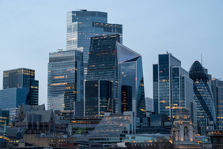 A landscape view of the City of London from the Tower Bridge. City of London skyline illuminated at dusk as seen from Tower Bridge. Office towers and landmarks along the River Thames glow against the night sky.