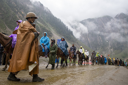 An India paramilitary soldier seen on guard as Hindu devotees make their way on foot, ride horses and are carried by porters along a mountain path during the annual Amarnath pilgrimage to the cave shrine in Baltal some 100 km (62 miles) east of Srinagar. Braving sub-zero temperatures and high-altitude mountain trails, thousands of Hindu devotees have begun the annual Amarnath Yatra pilgrimage across the Himalayas of Indian-administered Kashmir to reach the sacred Amarnath cave, which houses a naturally formed ice stalagmite revered as a symbol of Lord Shiva. Running from July 3 to August 28, 2026, the holy journey is heavily guarded by thousands of security personnel across both the traditional Pahalgam and steeper Baltal routes, even as environmental experts warn that surging crowds and heavy reliance on diesel generators are placing critical pressure on the region's fragile, climate-threatened ecosystem.