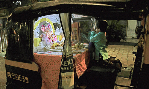A child kneeling on the driver's seat prays to the idol of elephant-headed Hindu god Ganesha installed on the passenger seat inside an autorickshaw in Mumbai. Satyawan Geete, approximately 52 years of age, an auto driver and a devotee of elephant-headed Hindu god Ganesha said he installed the idol of Ganesha inside his auto since last 11 years during the ten day festival of Ganesh Chaturthi which is celebrated across the country. he said that doing so gives him happiness when devotees come and pray and pay respect to the elephant-headed Hindu god Ganesha idol installed in his autorickshaw. He works hard the whole year and keeps aside some money from which he brings the idol, he goes around the city parking his auto around different pandals (temporary shelter) to give devotees a glimpse of his unique way of celebrating the festival and in his own words, he sings with karaoke and has been praised by print and digital media channels and on social media platforms, getting photographed with few celebrities making him a popular face on the streets of the city during the Ganesh Chaturthi festival.