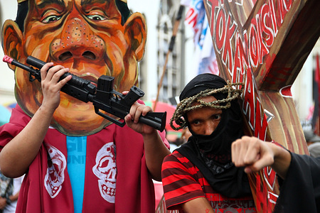 A protester carries a cross while an activist wear a Duterte mask mock and hit him as they march towards Mendiola bridge in Manila. Activists slammed Duterte for the alleged double standard in his war on drugs, the crackdown on activists, and the recent designation of activists as terrorists according to the Malacanang. The march was held a few days before the Holy Week, with protesters carrying a cross to Mendiola, Manila.