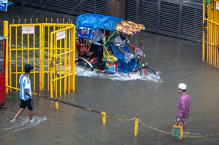 People struggle to walk through a waterlogged street following heavy rains causing much suffering for pedestrians and commuters. Monsoon downpour made travel slow and dangerous.