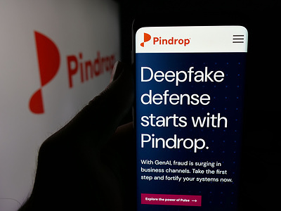 In this photo illustration, a person is holding a smartphone with the web page of US fraud detection company Pindrop Security on screen in front of logo.