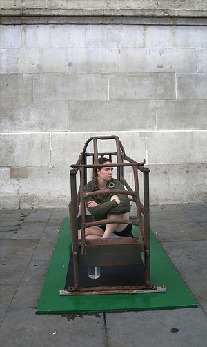 Michelle Farnham seen sitting inside her pig farrowing crate on day eleven of her protest in Trafalgar Square. Animal Rising activist Michelle Farnham reached the 11th day of her 21-day continuous lock-in inside a narrow pig farrowing crate set up in Trafalgar Square. The milestone demonstration was interrupted when Metropolitan Police officers responded to an incident involving a bystander throwing a liquid substance onto the installation, resulting in an arrest for criminal damage, while Farnham safely remained inside to highlight factory-farming conditions.