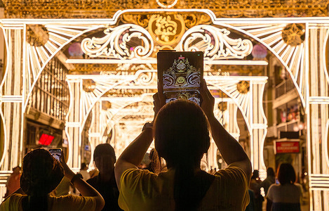 A visitor is using a tablet to record a video of the 'Phingkarat Phakdi, Long Live His Majesty the King' illuminated arch, installed to promote tourism from the Yi Peng Festival to the Lanna New Year at Thapae Gate. The "Phingkarat Phakdi, Long Live His Majesty the King" illuminated arch at Thapae Gate symbolizes the loyalty and gratitude of the people of Chiang Mai toward His Majesty the King, wishing him a long and prosperous reign. Organized by the Chiang Mai Municipality, this project aims to promote local tourism and the economy, offering both Chiang Mai residents and tourists the opportunity to experience the city's beauty during the festive season, from the Yi Peng Festival to the Lanna New Year Festival.