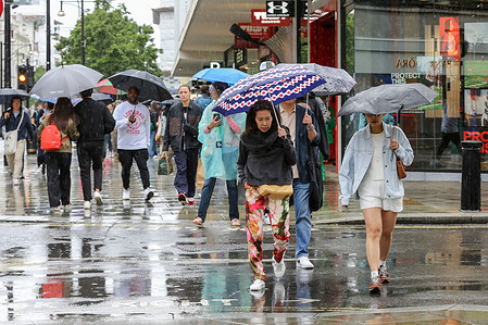 Members of the public shelter under umbrellas during rainfall in London.