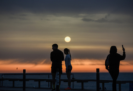 People seen during sunrise behind a thin veil of morning clouds in the early sky.