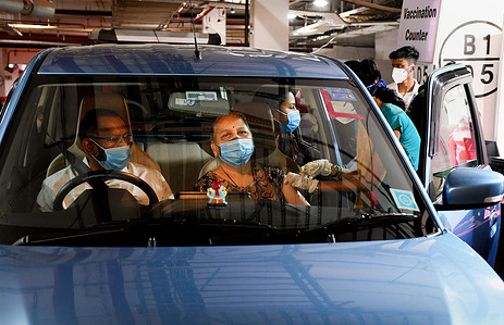 A healthcare worker wearing a face mask administers a COVID19 vaccine dose to a woman inside her car at Kohinoor public parking in Mumbai.This facility is opened to cater to senior citizens and differently abled people.