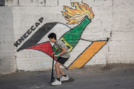 A Palestinian boy seen on a scooter passing next to a mural painted in support and appreciation of Northern Irish rap trio Kneecap, in Aida refugee camp. The Northern Irish rap trio Kneecap has been fundraising and supporting the ACLAÍ Palestine gym, in the Lajee Cultural Centre, in Aida refugee camp, since it opened in 2020. It has been offering support for Palestinians and is against the siege and bombardment of Gaza.