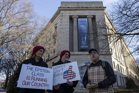 Protesters hold signs as a large banner featuring U.S. President Donald Trump and the slogan “Make America Safe Again” is displayed on the exterior of the United States Department of Justice headquarters. The banner was installed on Thursday outside the department’s main building.