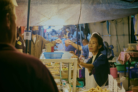 The woman at the market attentively listens to a customer who is eager to place an order. Thai street food night market in Chiang Rai