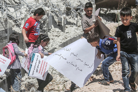 Palestinian students hold placards on the rubble of their destroyed aqaba mixed basic school protesting against its demolition by Israeli forces in the village of Aqaba in the northern Jordan Valley, north of the occupied West Bank.
