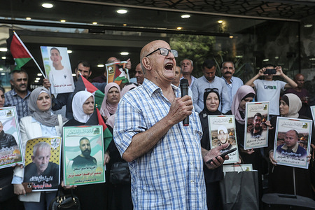 A man chants slogans through a microphone as families of Palestinian prisoners hold photos of their imprisoned relatives during a solidarity rally. Palestinians staged a protest to demand a prisoner exchange agreement with the Israeli government and Hamas.