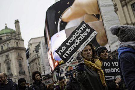 A protester holds a placard saying "No vaccine mandates" as she walks past Piccadilly Circus during the demonstration.Protesters marched through central London during a worldwide rally for freedom - protesting against government restrictions surrounding Covid 19 including mandatory vaccinations, particularly with NHS staff, who may face losing their job if they refuse to get vaccinated.
