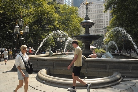 People walk past a fountain in City Hall Park in Manhattan, New York City.