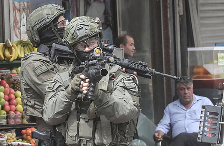 Israeli soldiers aim their weapons towards Palestinians and take up positions in the middle of a market. Israeli forces raided the central market and several gold and money exchange shops alleging they are dealing with Hamas. Clashes and stone-throwing erupted between Palestinian youths and Israeli forces resulting in the death of one Palestinian and the injury of others.