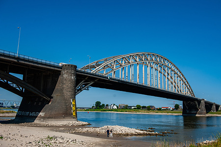 People seen walking over an area that is normally covered by the river. The low water level in the Waal River a result of prolonged drought and reduced glacial meltwater in the Rhine. Due to the increasing drought, houseboats are lying on the muddy bottom in the Ooijpolder area. According to waterpeilen.nl, the Rhine discharged an average of 1,150 cubic meters of water per second in June approximately 50 percent less than usual. Near the footbridge, stones and objects that normally lie underwater are reappearing.