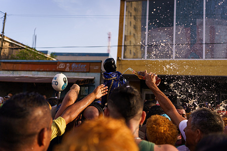 The crowd is seen throwing rum at the statue with the Cabimas cathedral in the background. The San Benito festival is celebrated in Cabimas within the Zulia state every December 27th. The celebration involves a significant procession spanning over 13 kilometers through the city, where devotees carry the saint's statue. Thousands of participants join in, chanting, playing music, and symbolically offering rum to the statue as an act of devotion and to seek blessings and favors from the saint.