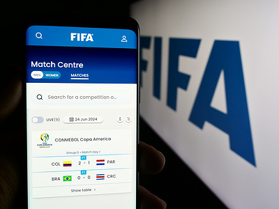In this photo illustration, a person is holding a mobile phone with the web page of Federation Internationale de Football Association (FIFA) with logo.