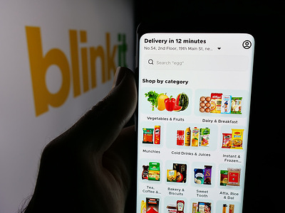 In this photo illustration, a person is holding a smartphone with the webpage of Indian company Blinkit (Blink Commerce) on screen in front of logo.