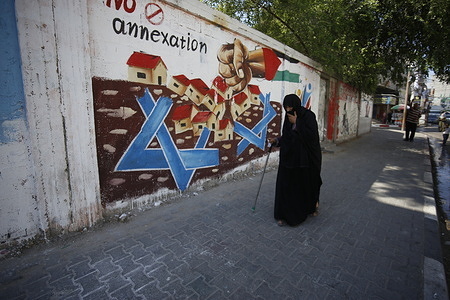 An elderly Palestinian woman walks past a protest mural of Israel's plan to annex parts of the Israeli-occupied West Bank, in Rafah in the southern Gaza Strip.