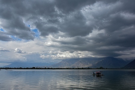 A boatman ferries tourists across the world famous Dal lake during a cloudy day in Srinagar. Erratic weather conditions continued to grip Kashmir valley with widespread rainfall across the plains and fresh snowfall in higher reaches. The adverse conditions triggered a major landslide, forcing the closure of all key road links connecting the Valley with the rest of the country.