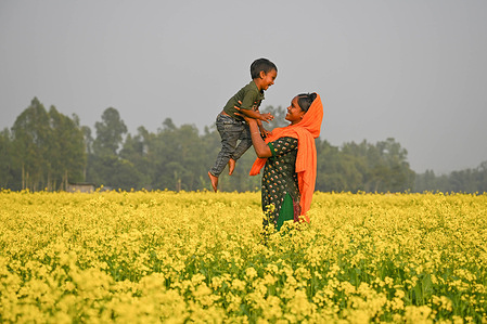 A mother plays with her child amid a blooming mustard field.