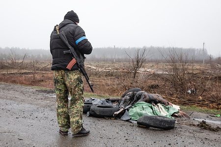 (EDITORS NOTE: Image depicts death) A civilian defence force look at four dead civilians on the sidelines of the highway under a blanket at 20km from Kyiv. Almost 300 civilians have been killed along the road in between Mriia and Myla on E40 highway as most victims tried to cross the Buchanka river to reach the Ukrainian controlled territory and had been killed. Russia invaded Ukraine on 24 February 2022, triggering the largest military attack in Europe since World War II.