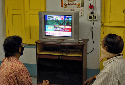 In this photo illustration an old couple seen watching the Lockdown extension news on a television while wearing face masks as a precaution against covid-19.