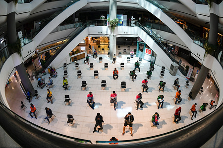 BANGKOK, THAILAND - MARCH 27, 2020:
People practice social distancing as they sit on chairs spread apart in a waiting area for take-away food orders at a shopping mall in hopes of preventing the spread of the coronavirus in Bangkok.