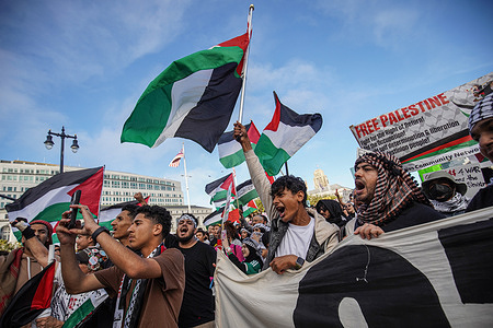 People demonstrate by yelling and waving the flags of Palestine outside the city hall. Over ten thousands people take to the streets of San Francisco to protest and call for an end to the latest Israel-Hamas war in the Middle East. The demonstrators hold placards, banners, and flags during the march, which starts at City Hall, proceeds down Market Street, and then returns to City Hall. This protest is part of the International Day of Solidarity to free Palestinians, and the protestors also demand an end to U.S. military aid to Israel. Similar demonstrations occur worldwide on the same day in solidarity with the Palestinian.